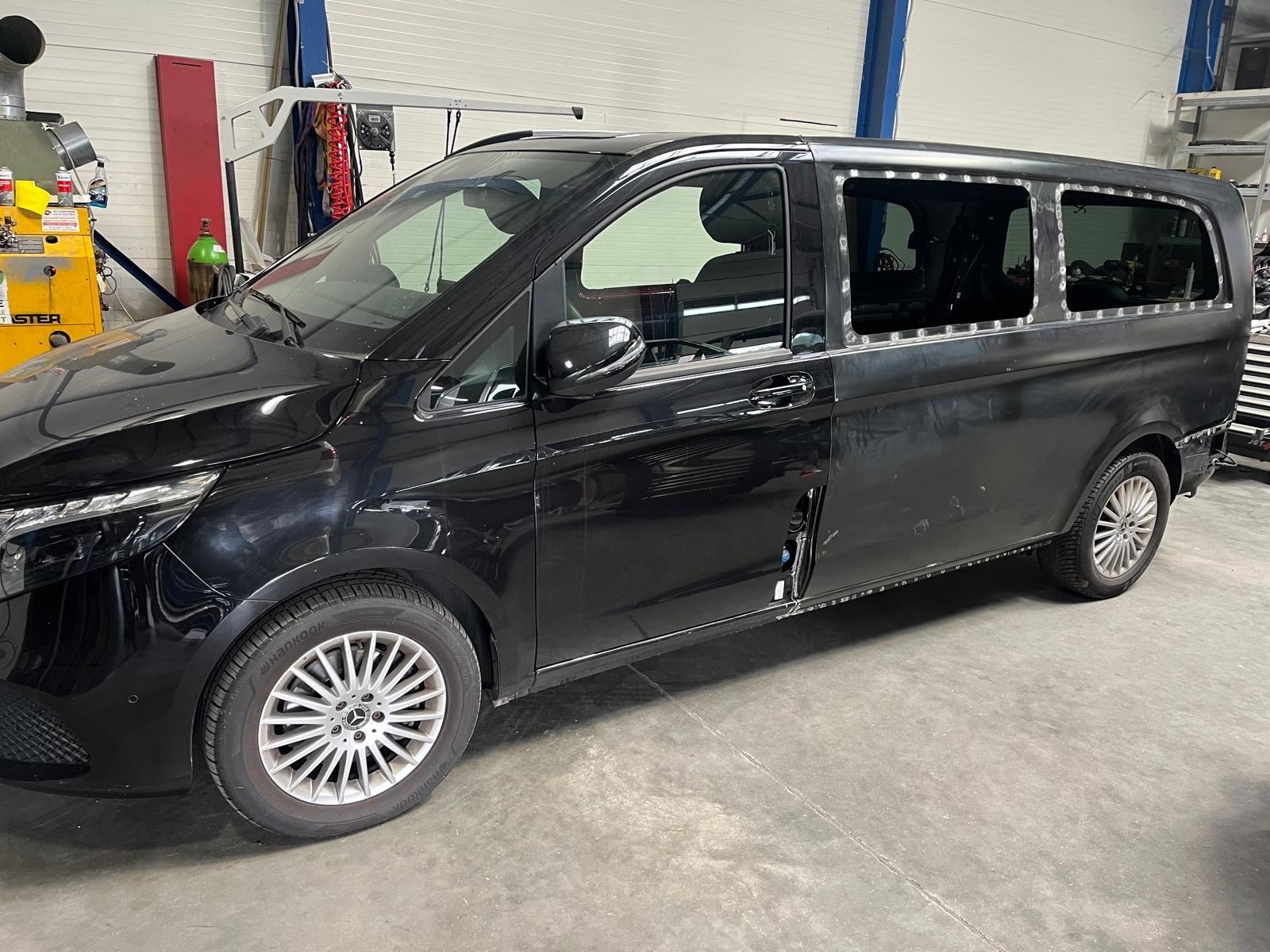 Czarny Mercedes Vito po przeróbkach karoserii, z wyciętymi otworami na okna boczne, widoczne ślady spawania. Prace blacharskie w warsztacie.