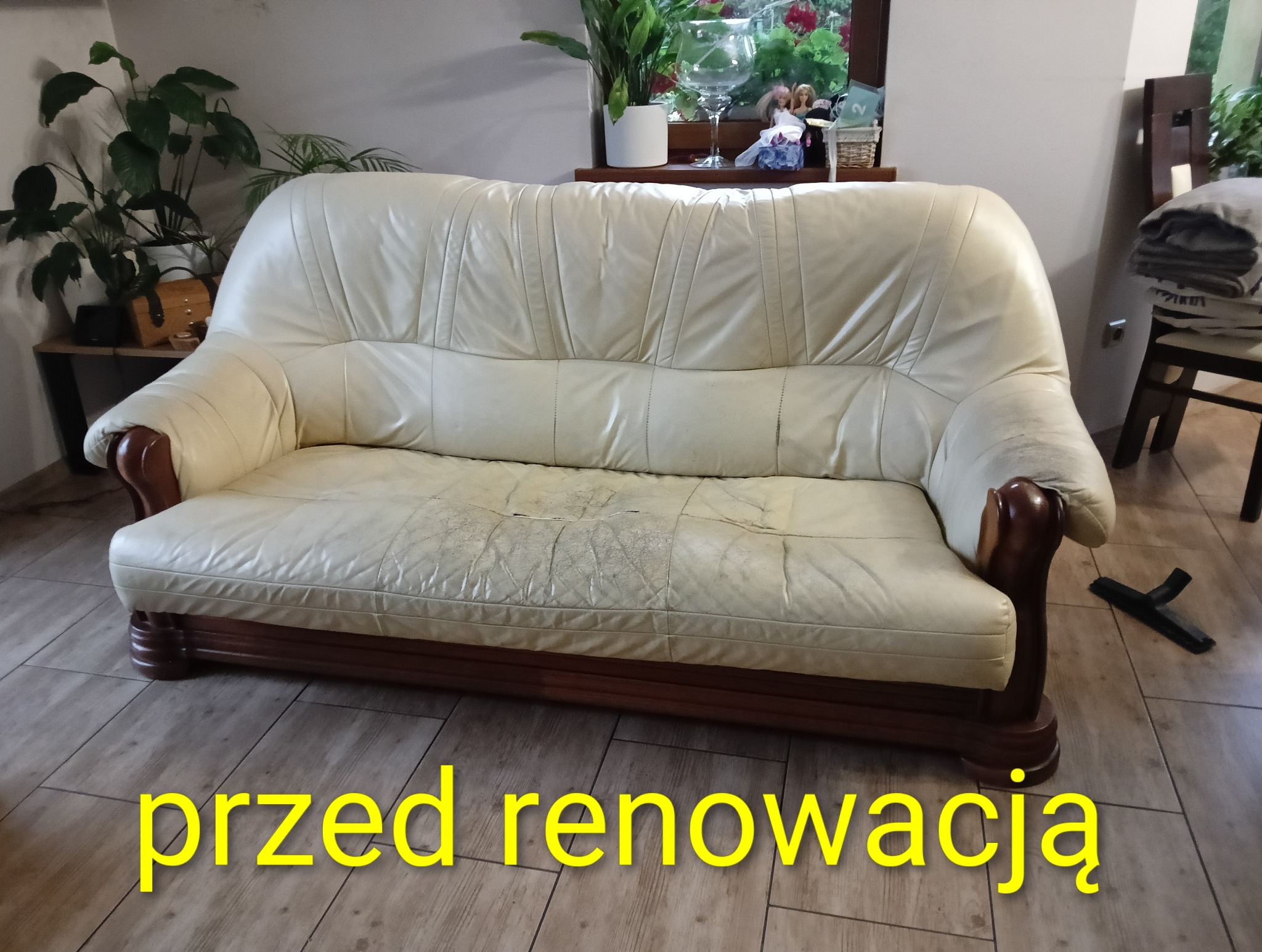 Kremowa sofa skórzana z widocznymi śladami użytkowania i przetarciami na siedzisku, drewniane wykończenia, w tle rośliny doniczkowe. Stan przed renowacją.