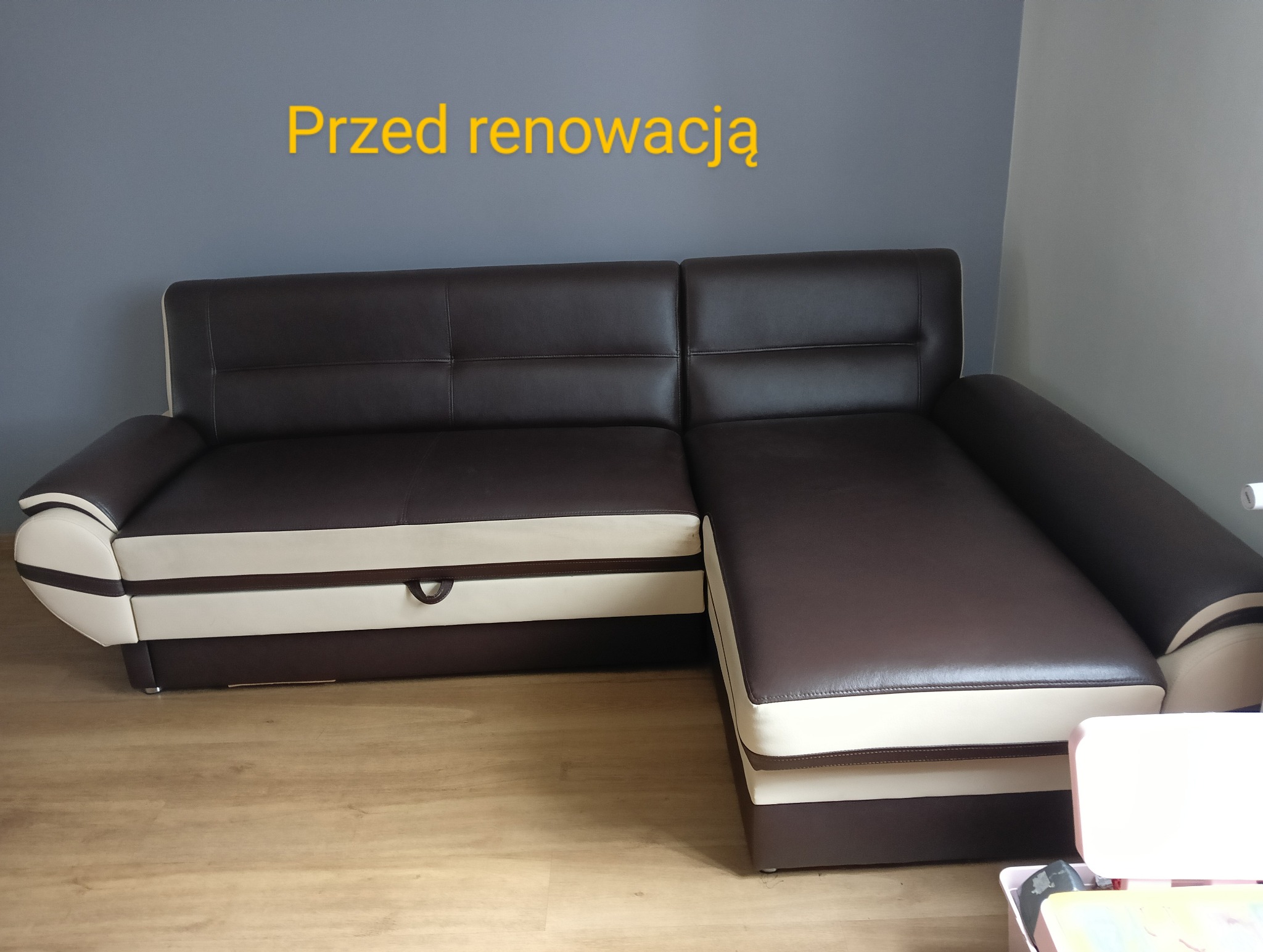 Brązowo-kremowa sofa narożna z widocznym schowkiem, sfotografowana z niskiego kąta, z napisem 'Przed renowacją' na szarej ścianie w tle.