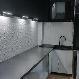 Majstereczek - Nowoczesna kuchnia z szarym blatem, białymi szafkami i wzorzystą ścianą. Czarna armatura i oświetlenie LED podkreślają minimalistyczny design.