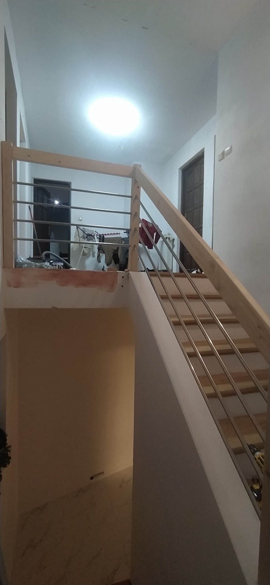 Nowe, drewniane schody z metalowymi barierkami w jasnym wnętrzu. Widoczne narzędzia i elementy wykończeniowe. Ujęcie z dołu, podkreślające konstrukcję.