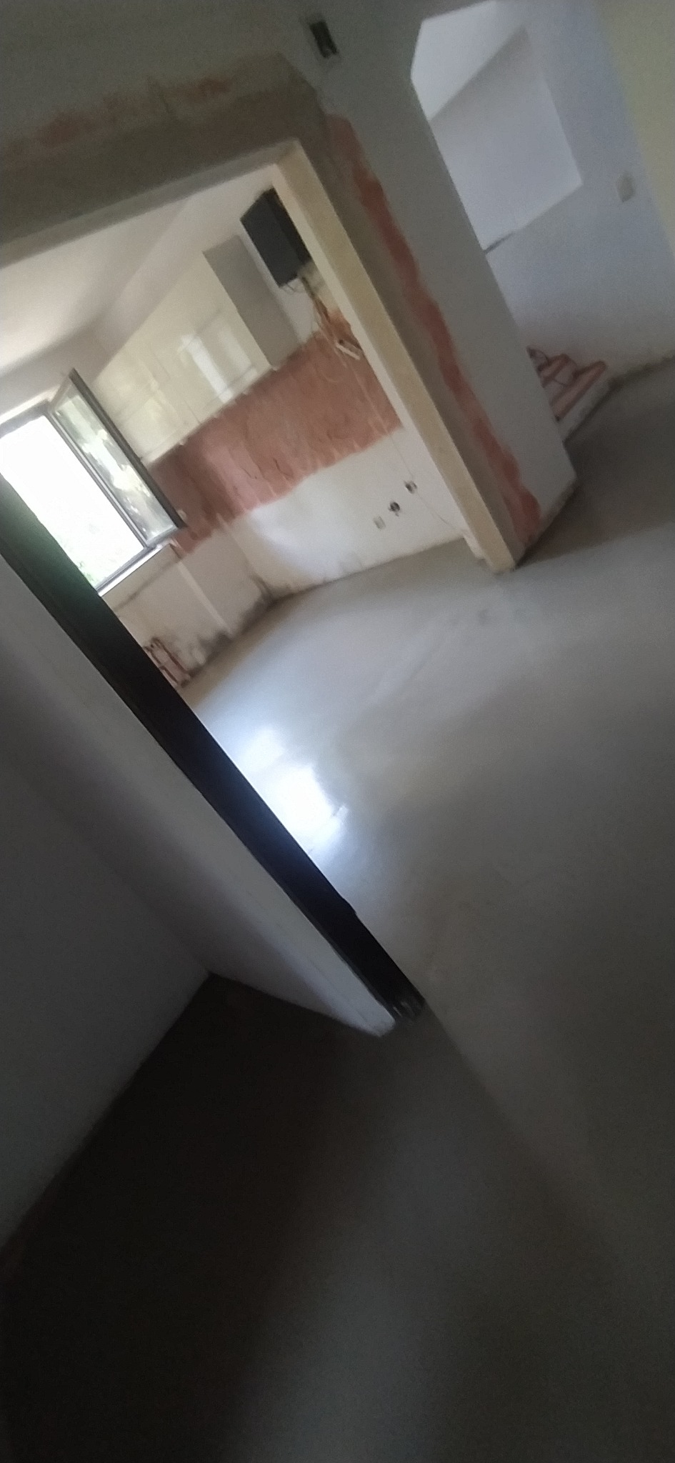 Wnętrze w trakcie prac wykończeniowych: wylewka podłogowa, ściany przygotowane do malowania, widoczne instalacje elektryczne. Ujęcie z nietypowej perspektywy.