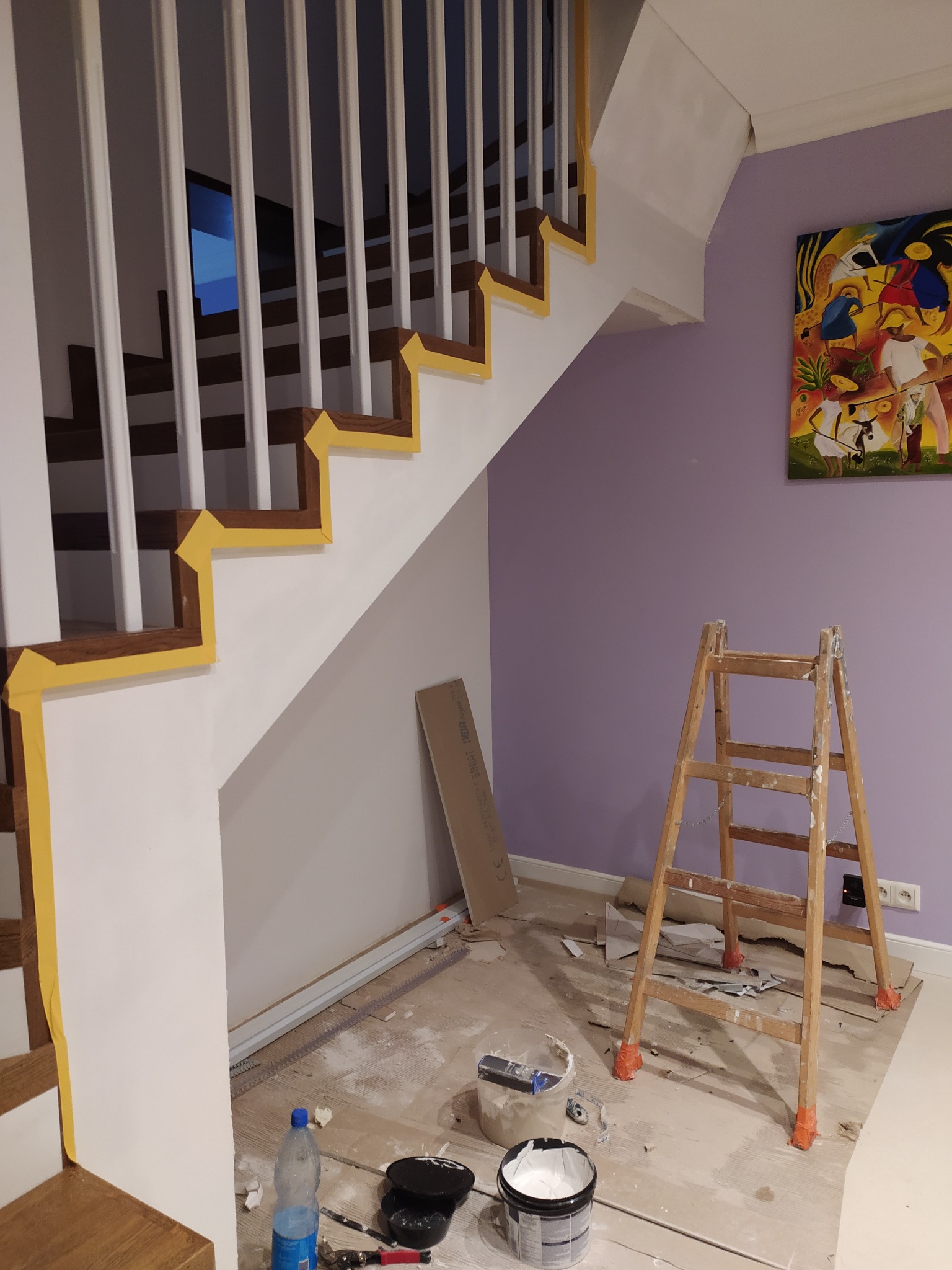 Malowanie schodów z zabezpieczeniem taśmą malarską, drabina oparta o fioletową ścianę, widoczne narzędzia i farby. Obraz na ścianie dodaje koloru.