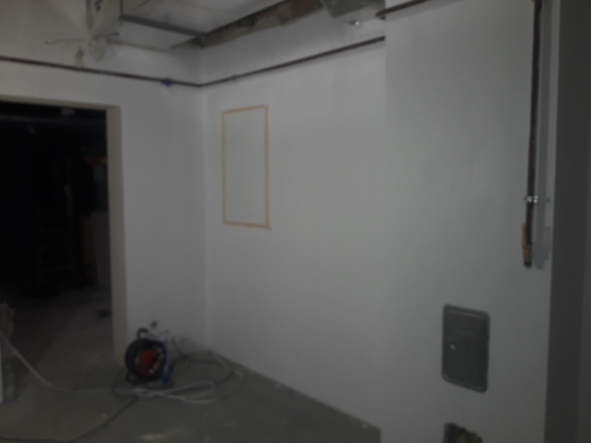 Wnętrze w trakcie prac wykończeniowych: świeżo pomalowane ściany na biało, widoczne instalacje elektryczne i otwór drzwiowy. Na podłodze leżą narzędzia.