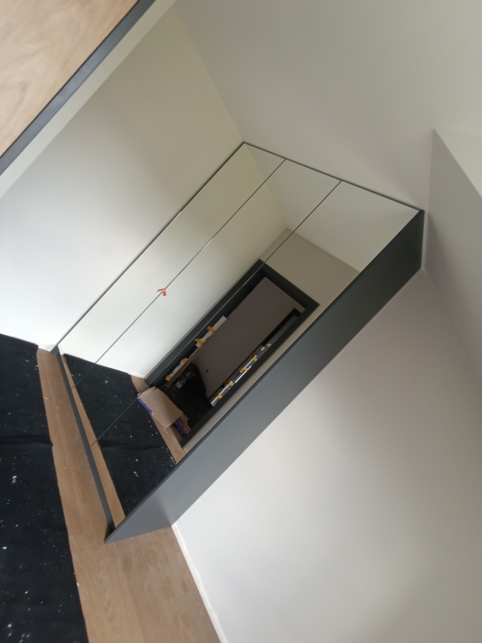 Szafa wnękowa z lustrzanymi drzwiami, widok z góry, ukazująca wnętrze z półkami i zawartością, w trakcie montażu, z widocznymi elementami wykończeniowymi.