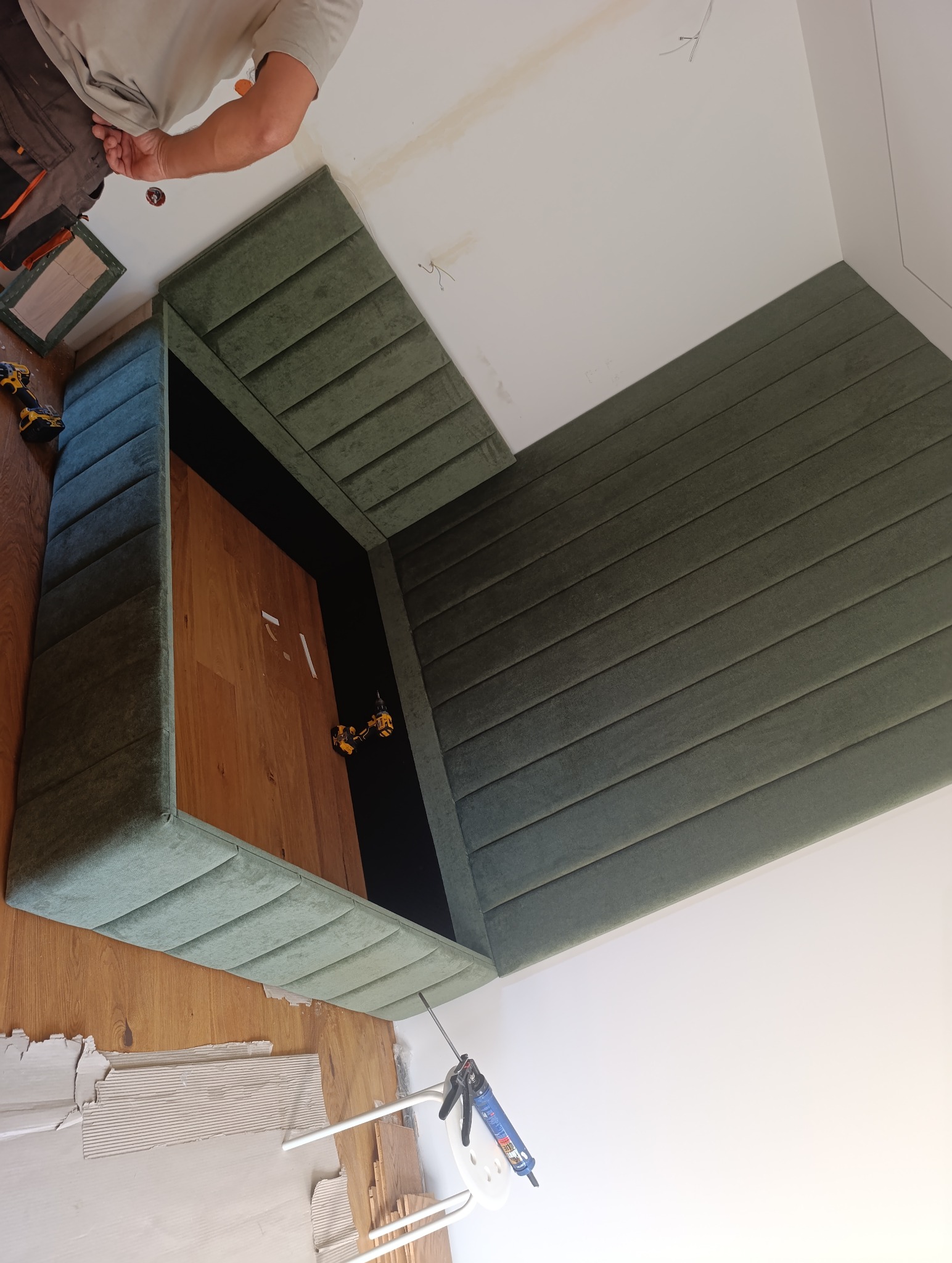 Montaż tapicerowanej szafy wnękowej z drewnianym dnem. Widoczny fragment sufitu, narzędzia pracy i klej. Ujęcie z dołu, podkreślające detale wykończenia.