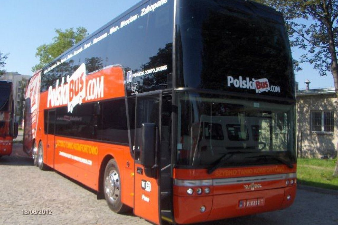 Pomarańczowy, dwupiętrowy autobus PolskiBus.com z widocznymi napisami 'Szybko Tanio Komfortowo' i adresem Facebook. Autobus stoi na parkingu w słoneczny dzień.