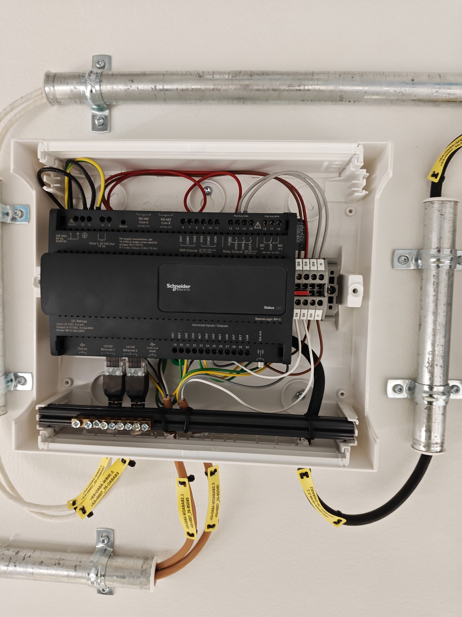 Rozdzielnica inteligentnego domu Schneider Electric z przewodami w rurkach instalacyjnych, zamontowana na ścianie. Widoczne oznaczenia przewodów.