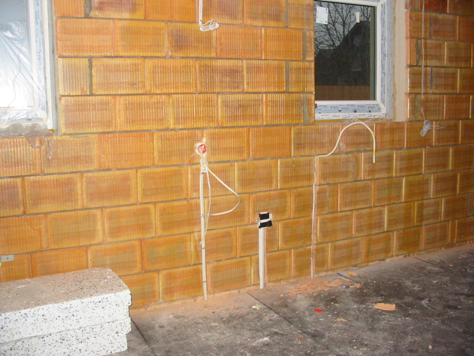 Ściana z pustaków z widocznymi przewodami elektrycznymi i puszkami instalacyjnymi. Okno w tle. Etap prac instalacyjnych w nowym budynku.