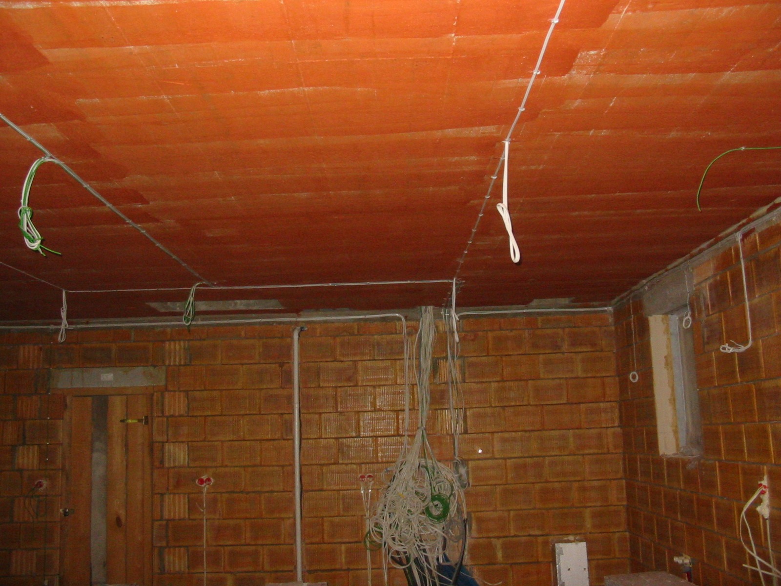 Ceglana ściana i pomarańczowy sufit z widocznymi przewodami elektrycznymi w trakcie montażu. Widoczne kable zwisające ze ściany i sufitu.