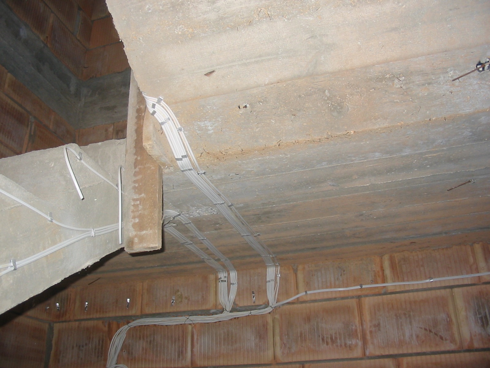 Szare kable elektryczne przymocowane do surowego betonowego sufitu i ceglanych ścian w trakcie budowy. Widoczne uchwyty mocujące kable.