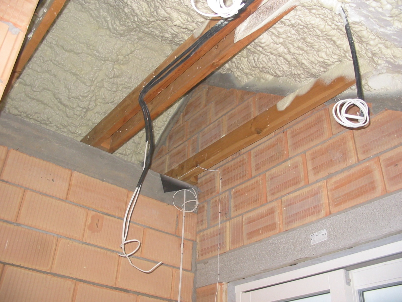 Ocieplenie pianą PUR poddasza z widocznymi przewodami elektrycznymi i fragmentem murowanej ściany z pustaków ceramicznych.