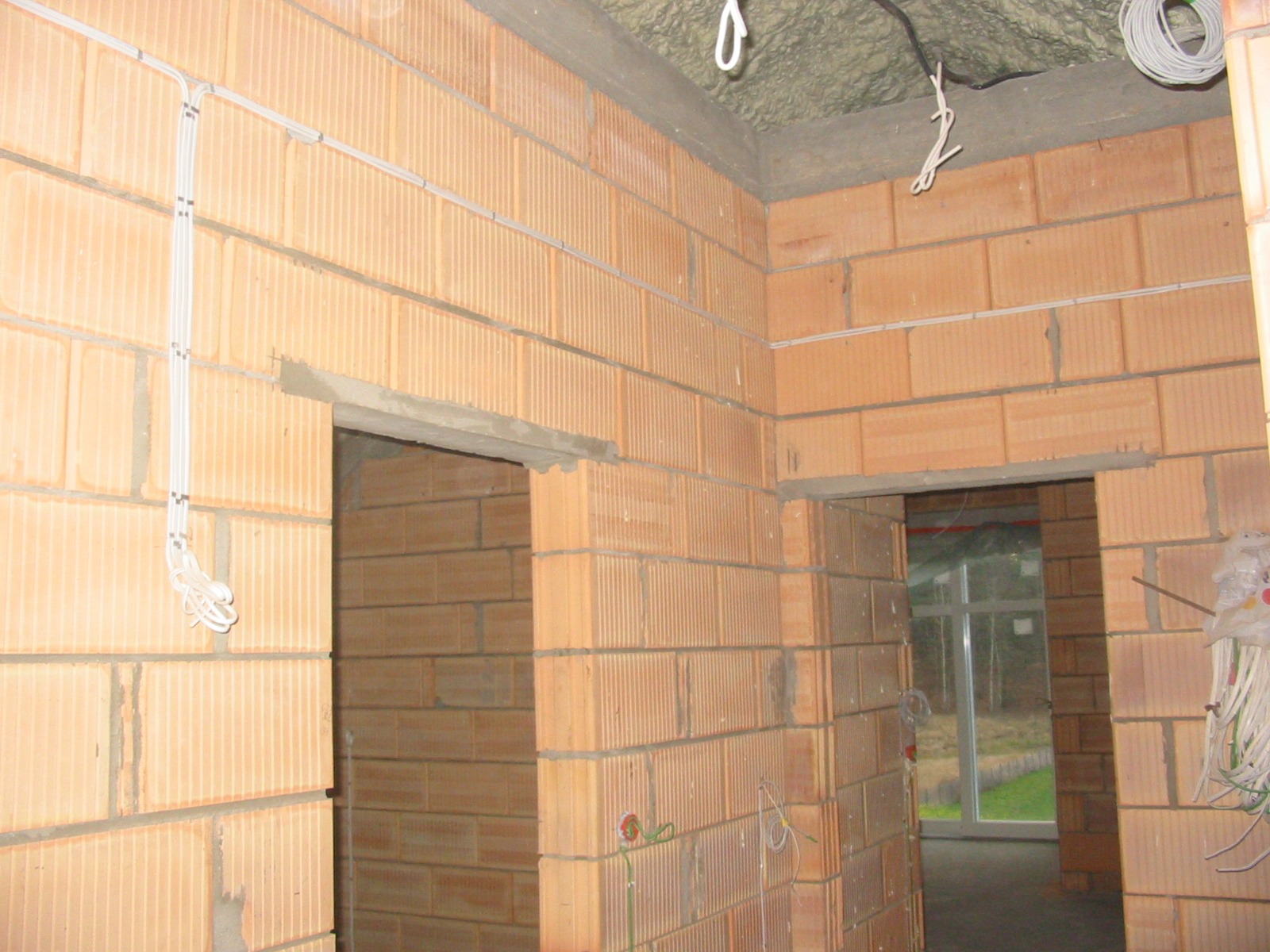 Instalacja elektryczna w surowym budynku z cegły. Widoczne przewody elektryczne prowadzone po ścianach, przygotowane do dalszych prac wykończeniowych.