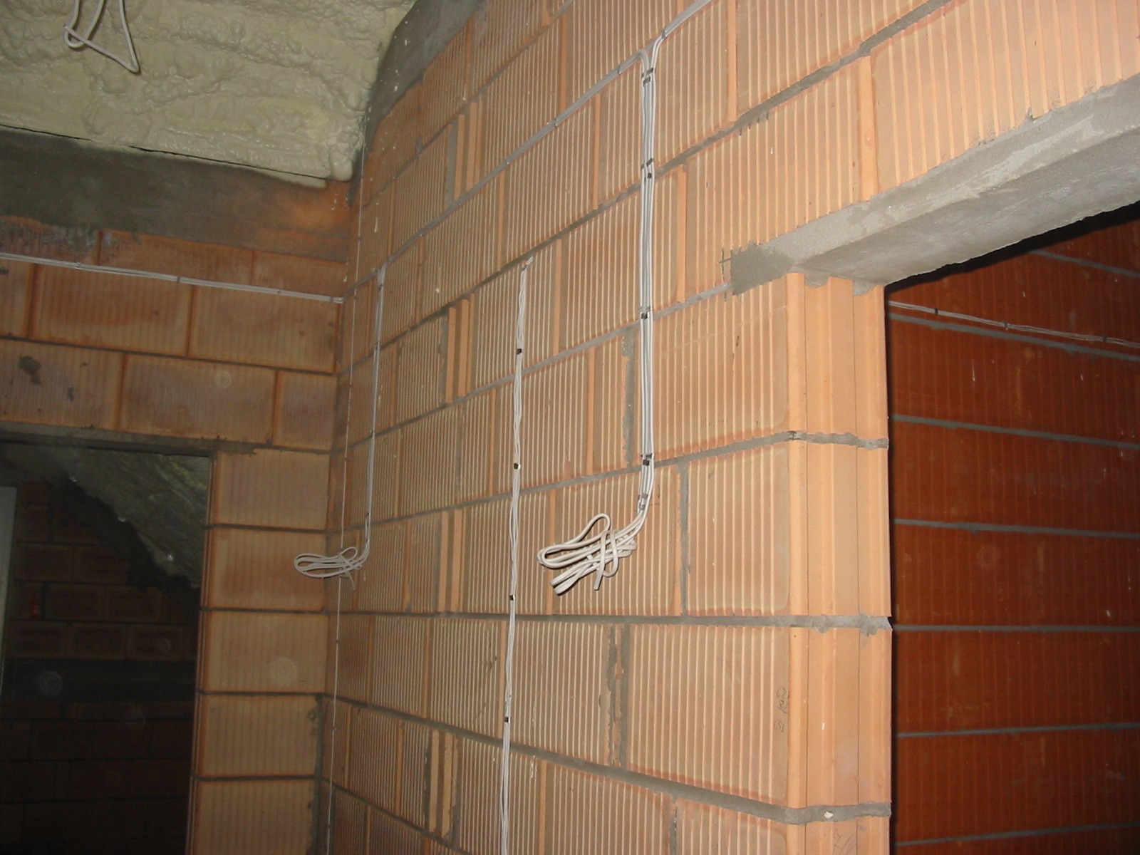 Wewnętrzne ściany z pustaków ceramicznych z rozprowadzoną instalacją elektryczną. Kable przymocowane do ściany, widoczne puszki instalacyjne. Surowy stan wykończenia.