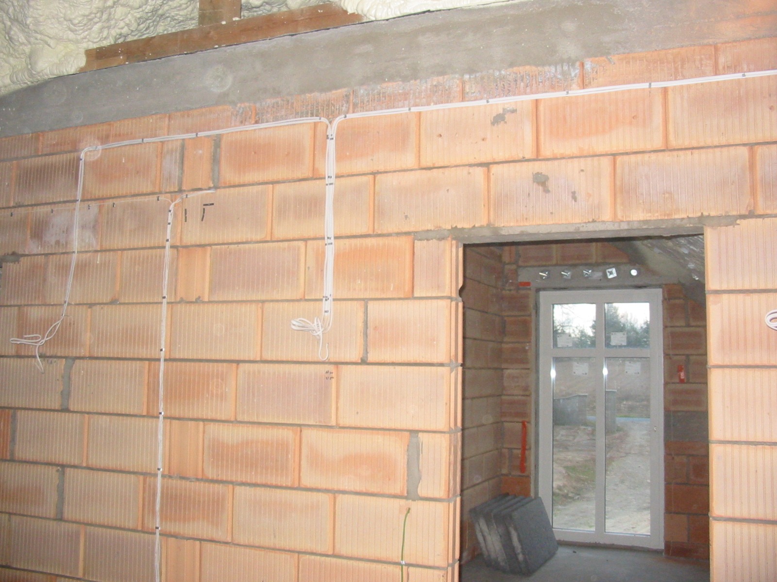 Ściana z cegieł z rozprowadzoną instalacją elektryczną w Garwolinie. Widoczne kable i puszki elektryczne przed tynkowaniem. Otwór okienny w tle.