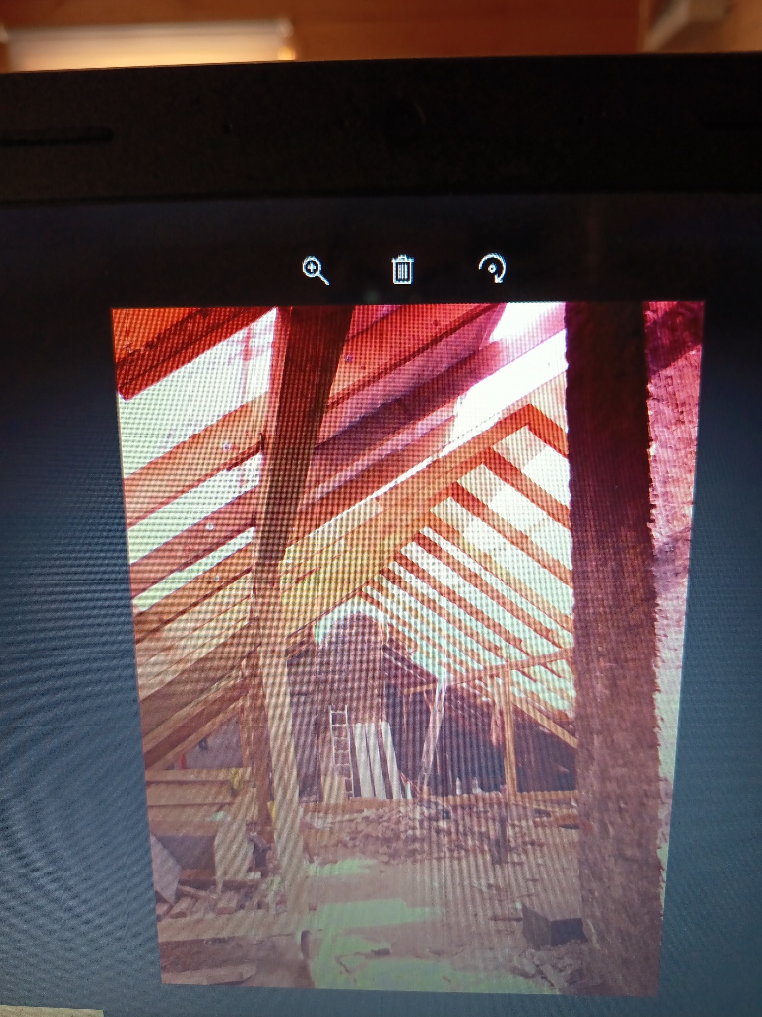 Konstrukcja dachu z drewnianymi belkami w trakcie budowy, widok z wnętrza poddasza. W tle komin i drabina. Surowe wykończenie, etap prac dekarskich.