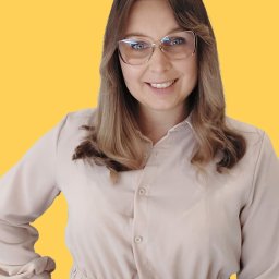 Uśmiechnięta kobieta w okularach, z rękami na biodrach, na żółtym tle. Profesjonalny wizerunek specjalisty z Brzózy, budzący zaufanie.