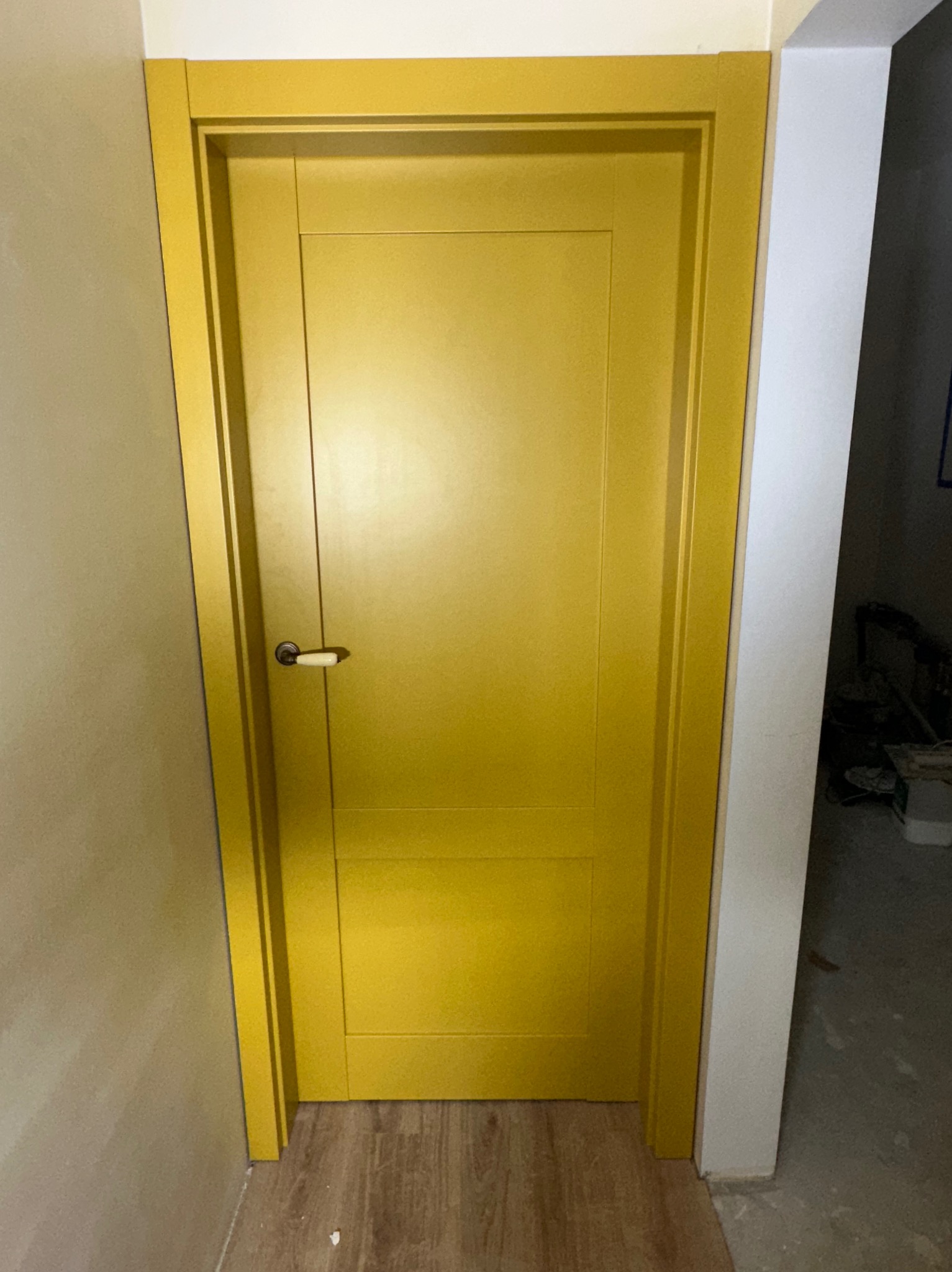 Żółte, nowoczesne drzwi wewnętrzne z klamką, zamontowane w ościeżnicy. Widoczny fragment podłogi i ściany. Minimalistyczny design.