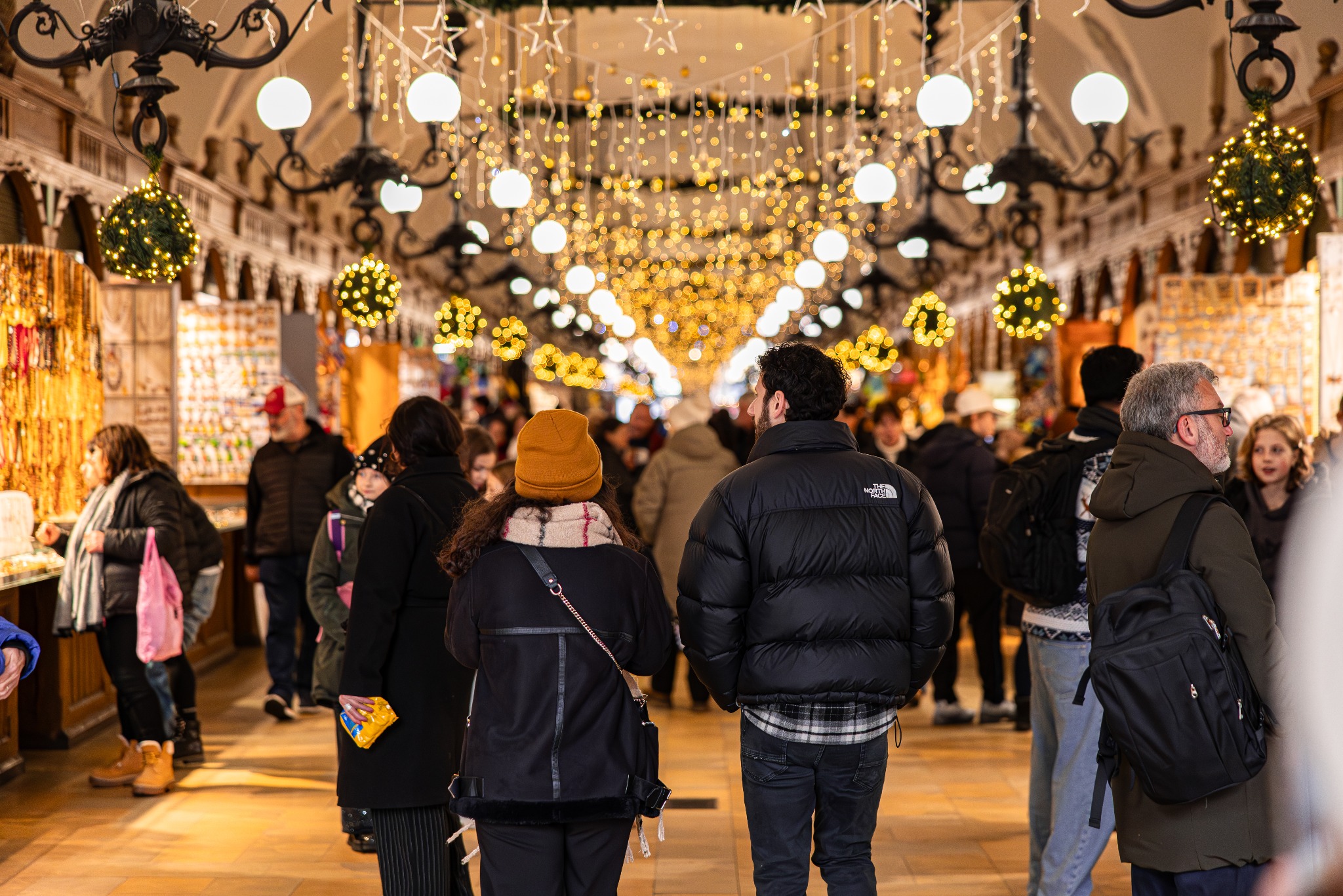 Tłum ludzi w hali targowej oświetlonej dekoracjami świątecznymi. Widok z perspektywy osoby stojącej w tłumie, skupiający się na parze idącej przed nią.