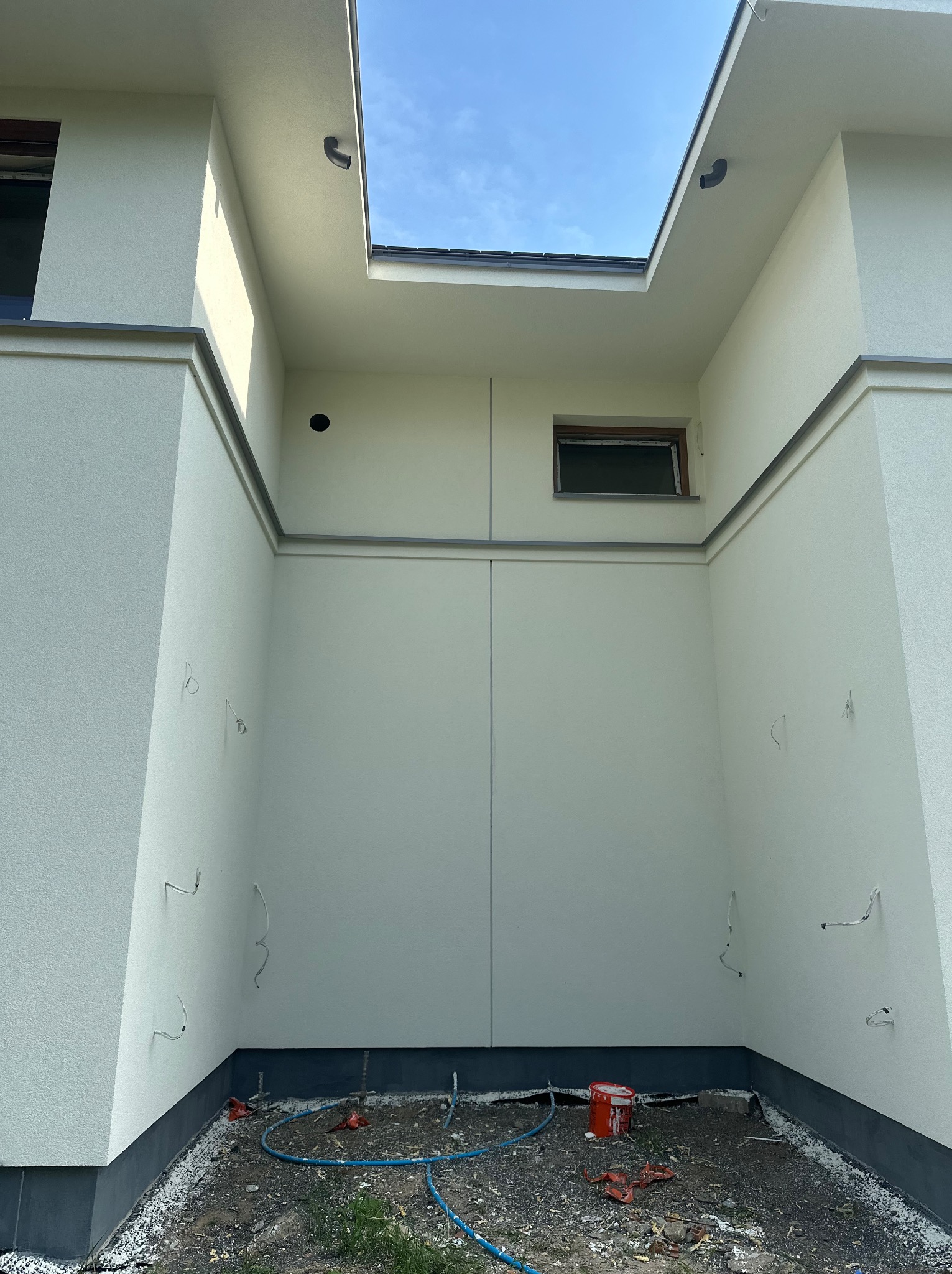 Jasna elewacja budynku z widocznymi przewodami i elementami wykończeniowymi. Ujęcie z dołu, podkreślające geometrię i detale architektoniczne. Widoczne niebo w górnej części kadru.