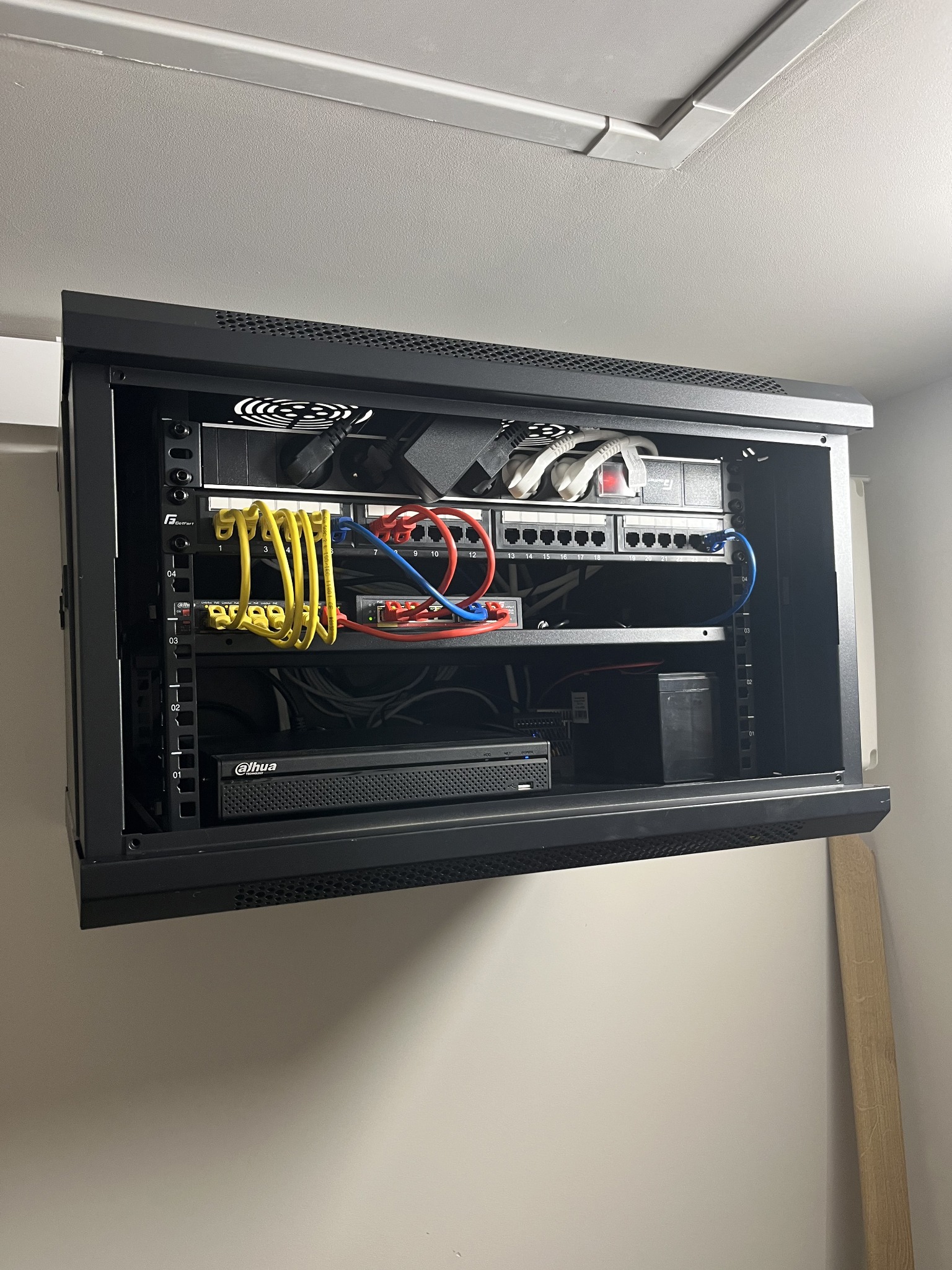 Zamknięta szafa rack z okablowaniem sieciowym, patch panelem, switchem i rejestratorem Dahua. Widoczne kable Ethernet w kolorach żółtym, czerwonym i niebieskim.