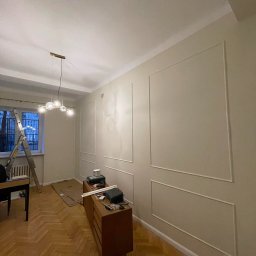 Adam Bujwicki - Pokój po dekoracyjnym malowaniu ścian z listwami, drewniana podłoga w jodełkę, drabina przy oknie, komoda z narzędziami. Widoczne ślady prac wykończeniowych.