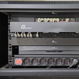 Squdo Technologies Michał Rus - Otwarta szafa rack z zamontowanym switchem, patch panelem, rejestratorem Dahua i listwą zasilającą. Widoczne kable i wtyczki. Sprzęt sieciowy GetFort.