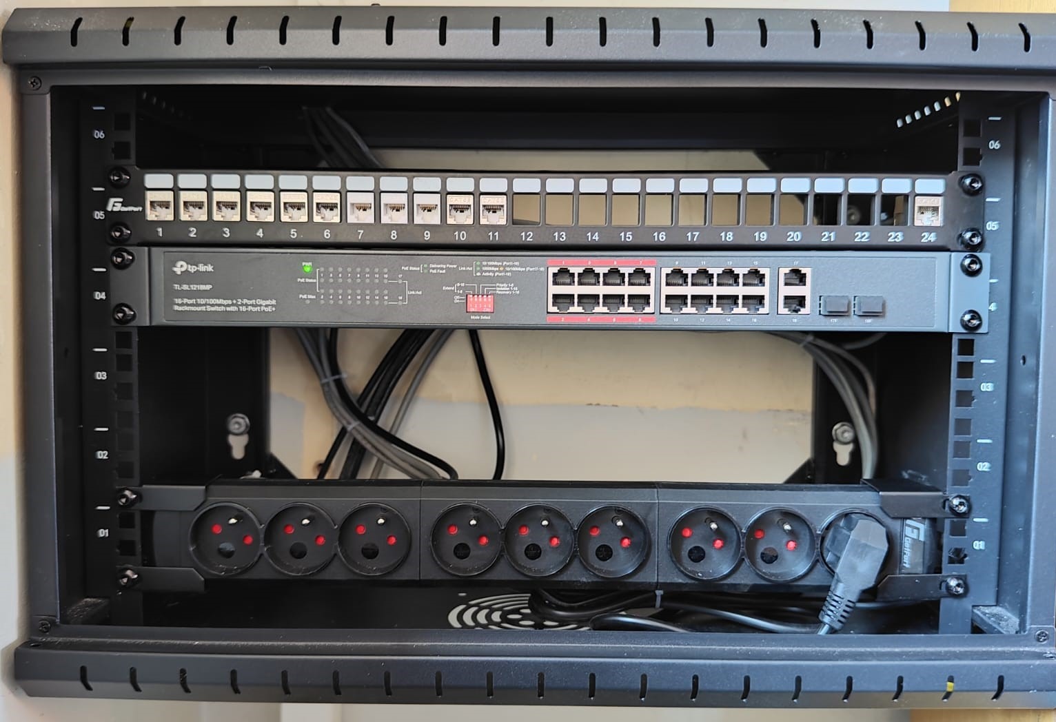 Szafa rack z patch panelem, switchem TP-Link i listwą zasilającą. Widoczne porty Ethernet i gniazda zasilania. Kable uporządkowane wewnątrz szafy.