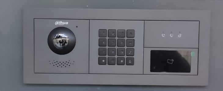 Panel domofonu Dahua z kamerą, klawiaturą numeryczną i czytnikiem kart zbliżeniowych, zamontowany na ścianie. Widoczne ikony połączeń i logo producenta.