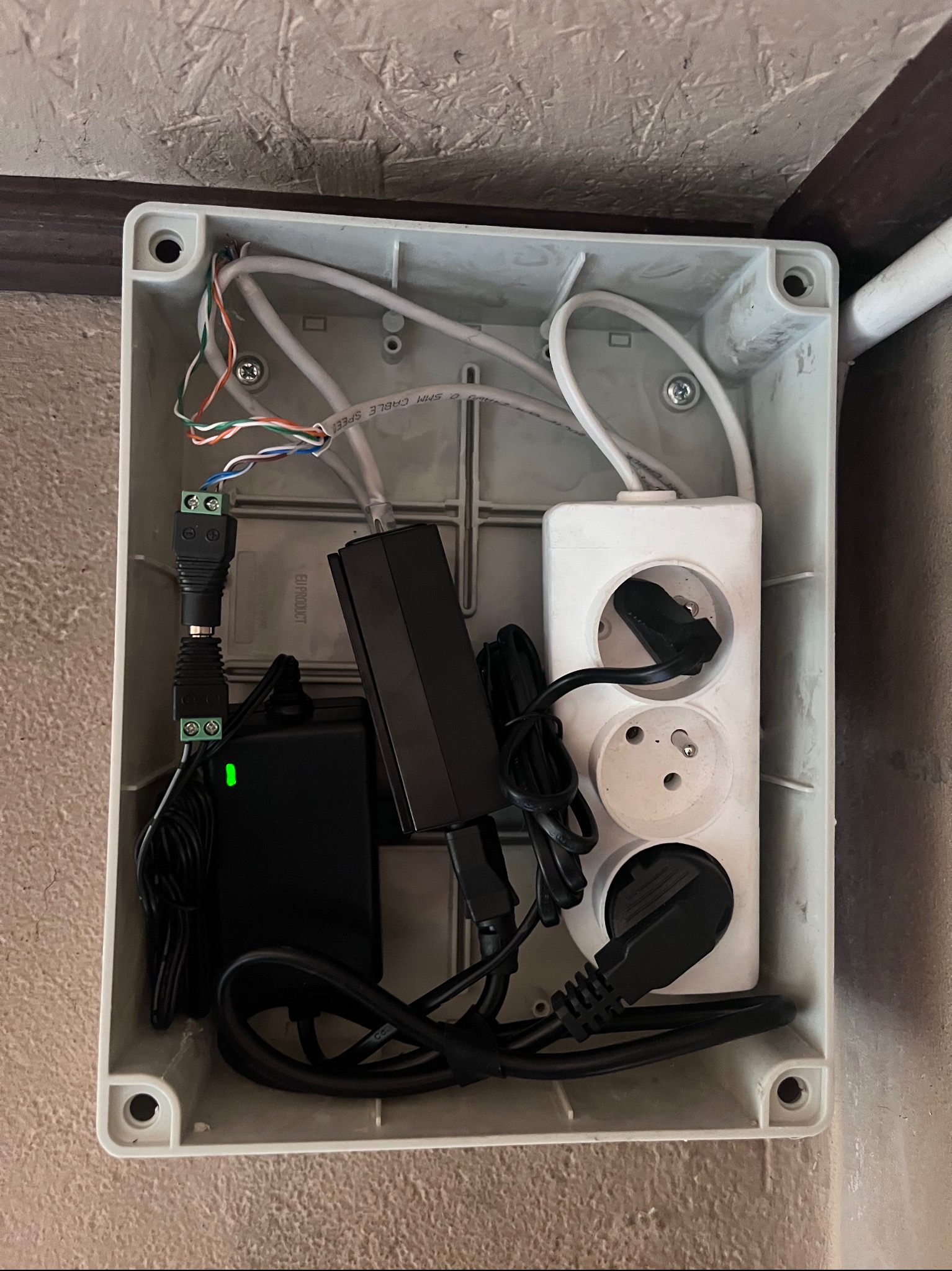 Szara skrzynka instalacyjna z przewodami, zasilaczami i listwą zasilającą. Widoczne kable, wtyczki i złącza. Instalacja elektryczna wewnątrz obudowy.