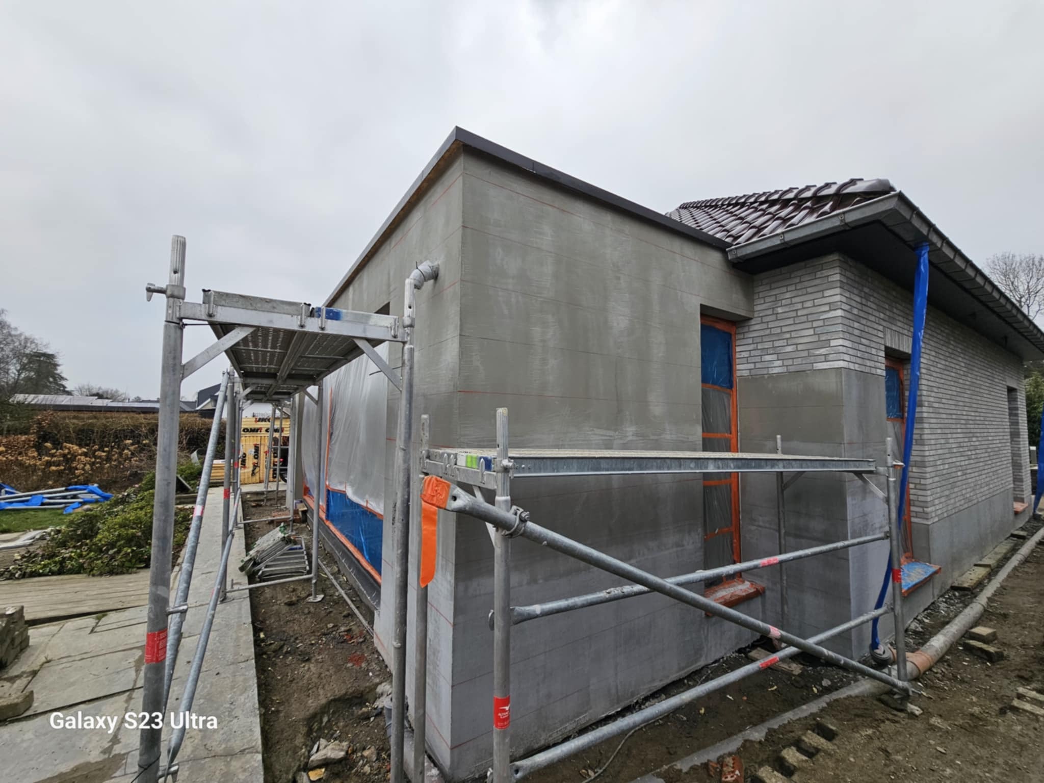 Ocieplanie elewacji domu jednorodzinnego w Urzędowie. Widoczne rusztowania i przygotowana powierzchnia pod tynk. Część budynku wykończona cegłą.