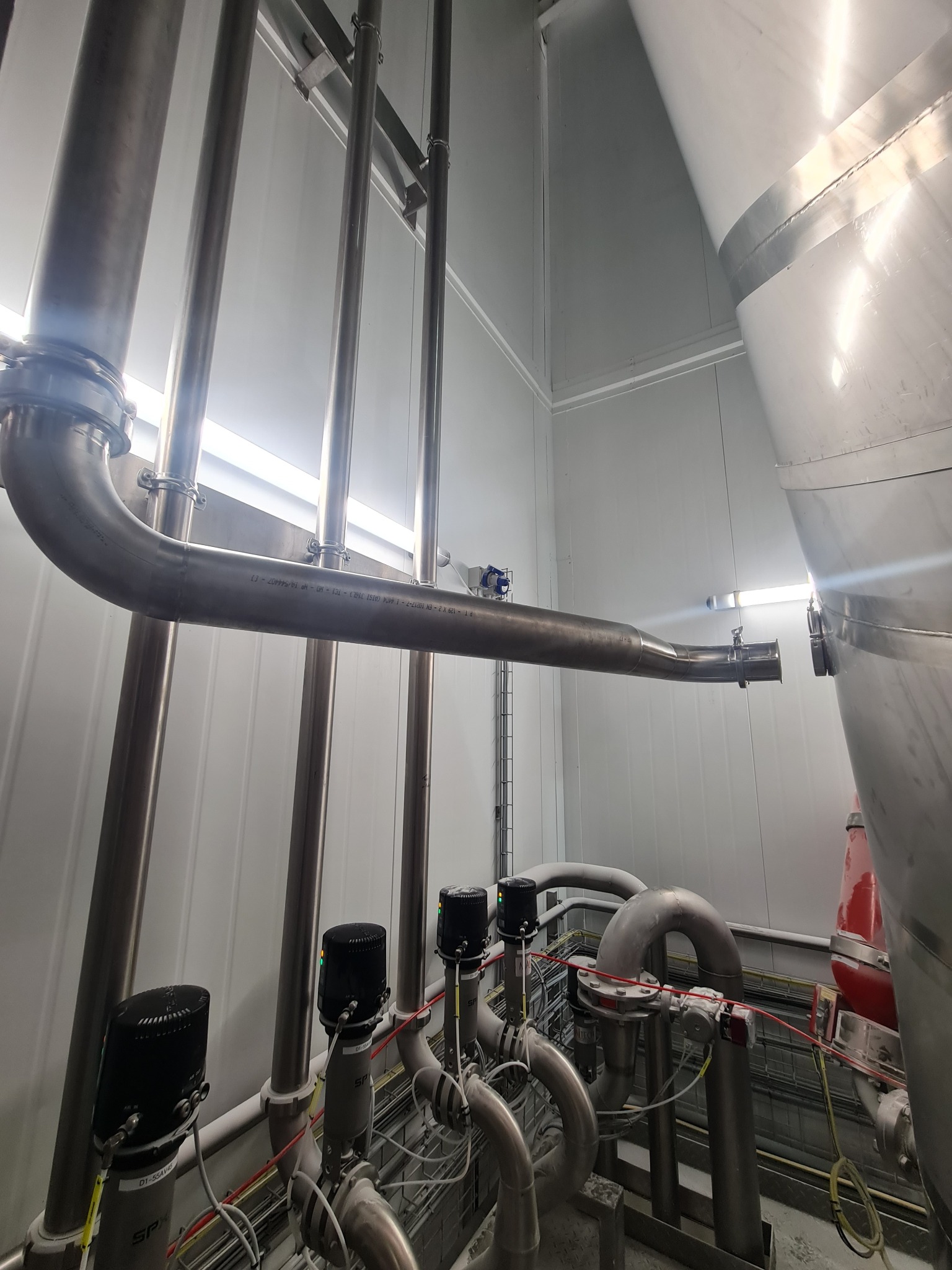 Kompleksowa instalacja rur ze stali nierdzewnej w sterylnym pomieszczeniu, z widocznymi zaworami, czujnikami i elementami mocującymi. Precyzyjne wykonanie, przemysłowy charakter.