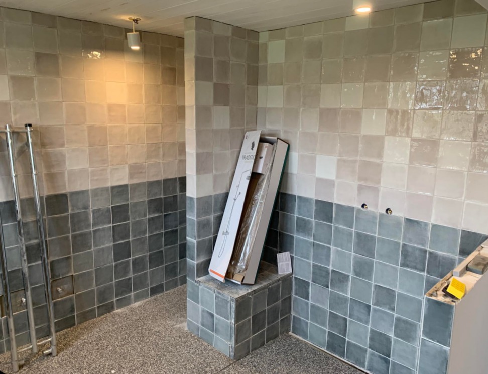 Wykończona łazienka z dwukolorowymi, kwadratowymi płytkami. Na pierwszym planie karton z zestawem prysznicowym. Widoczne narzędzia glazurnicze.