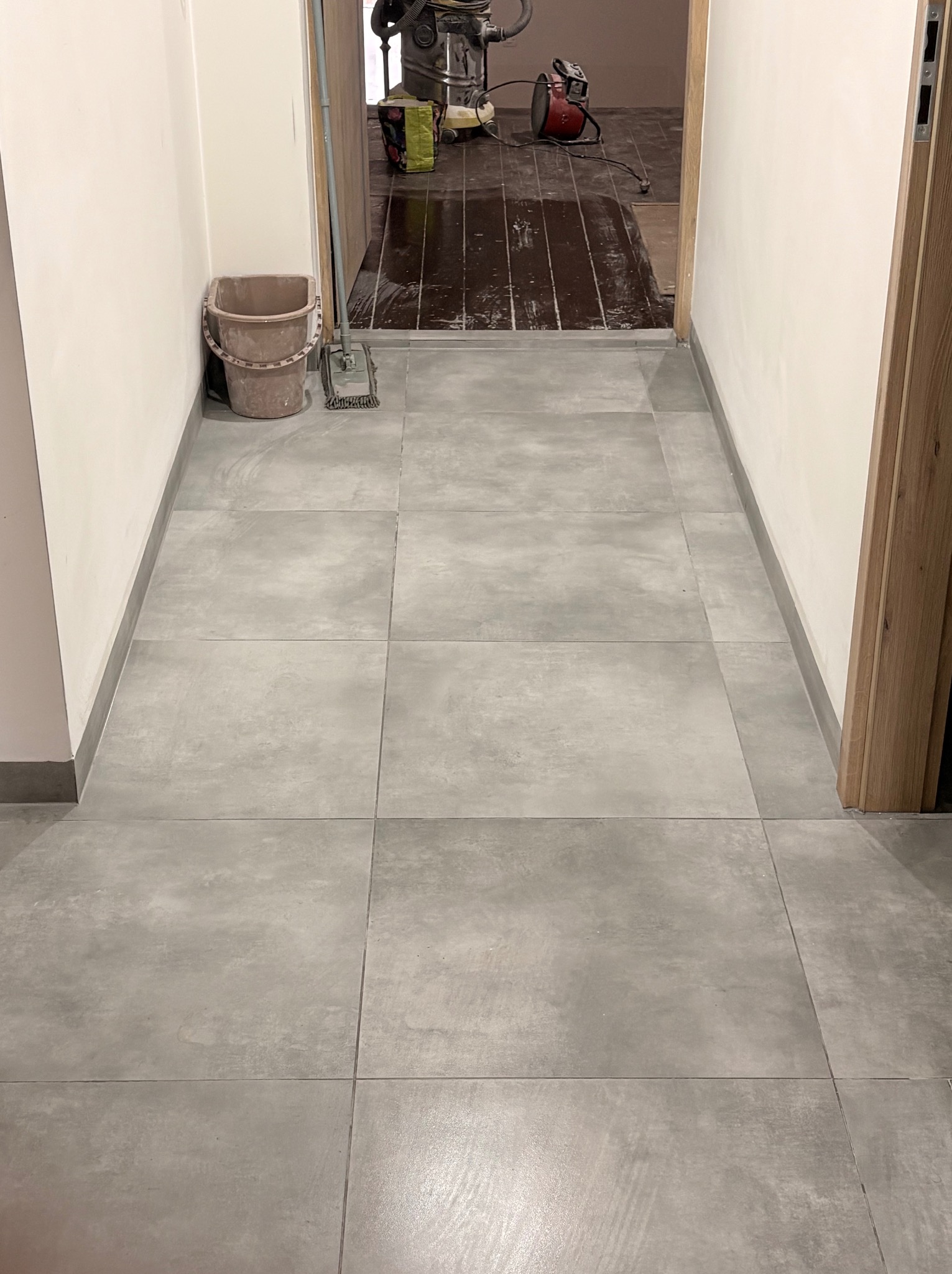 Ułożona szara, matowa terakota w korytarzu. W tle widoczne narzędzia i resztki po pracach wykończeniowych, co sugeruje świeżo zakończony etap prac.