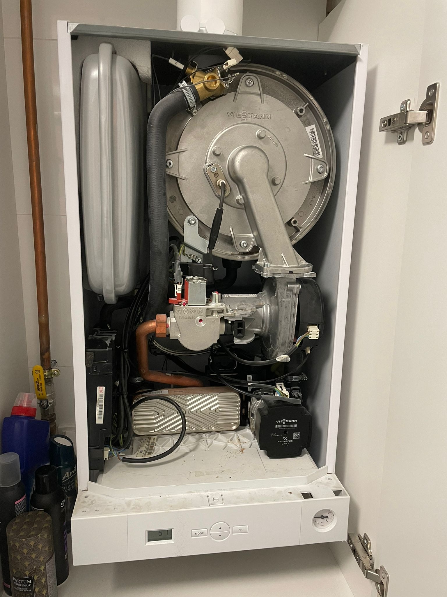 Otwarty piec gazowy Viessmann w białej obudowie, widoczne elementy wewnętrzne: palnik, wymiennik ciepła, rury miedziane i czarne przewody. Po lewej stronie widoczne kosmetyki.