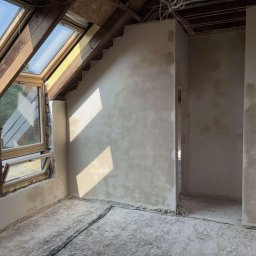 Łukasz Krawczyk - Poddasze po szpachlowaniu ścian, widoczne okna dachowe i surowe wykończenie podłogi. Ściany przygotowane do dalszych prac wykończeniowych, z widocznymi śladami szpachli.