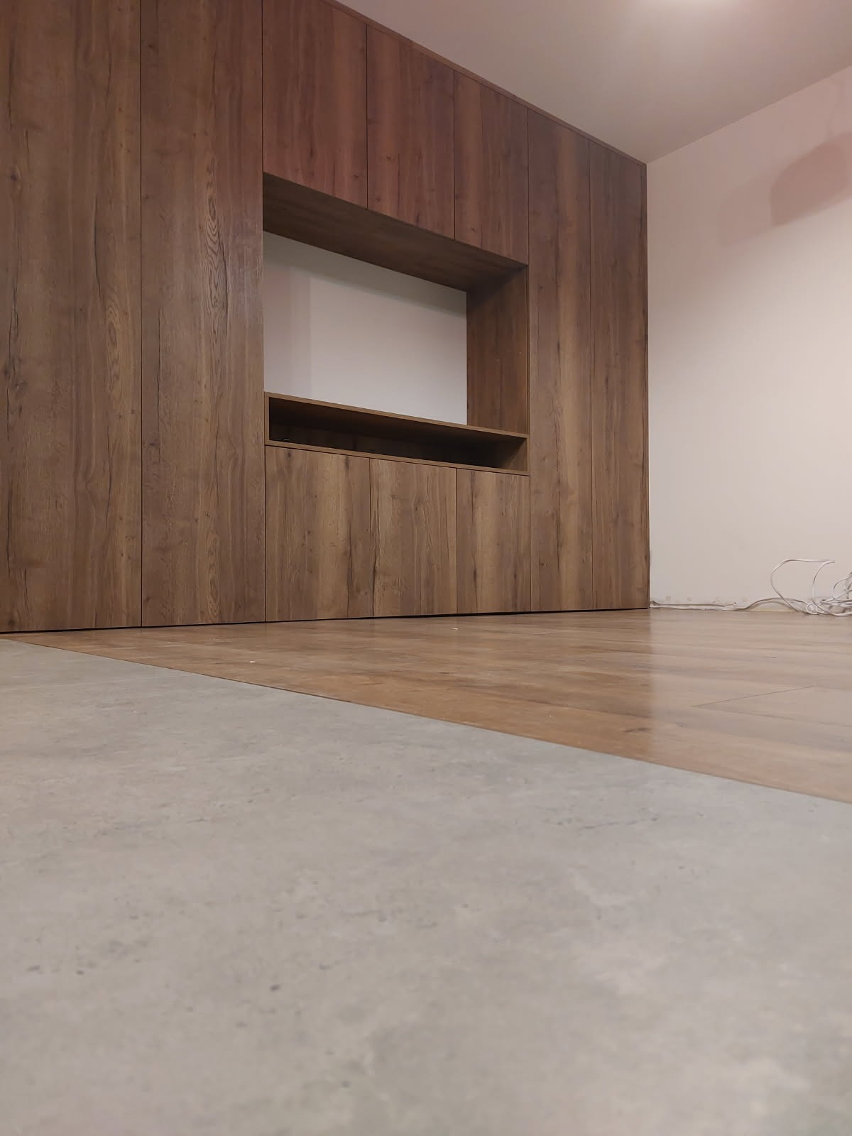 Drewniana szafa wnękowa z półką w salonie, widok z dołu, podkreślający strukturę drewna i minimalistyczny design. Nowoczesne wykończenie wnętrza.