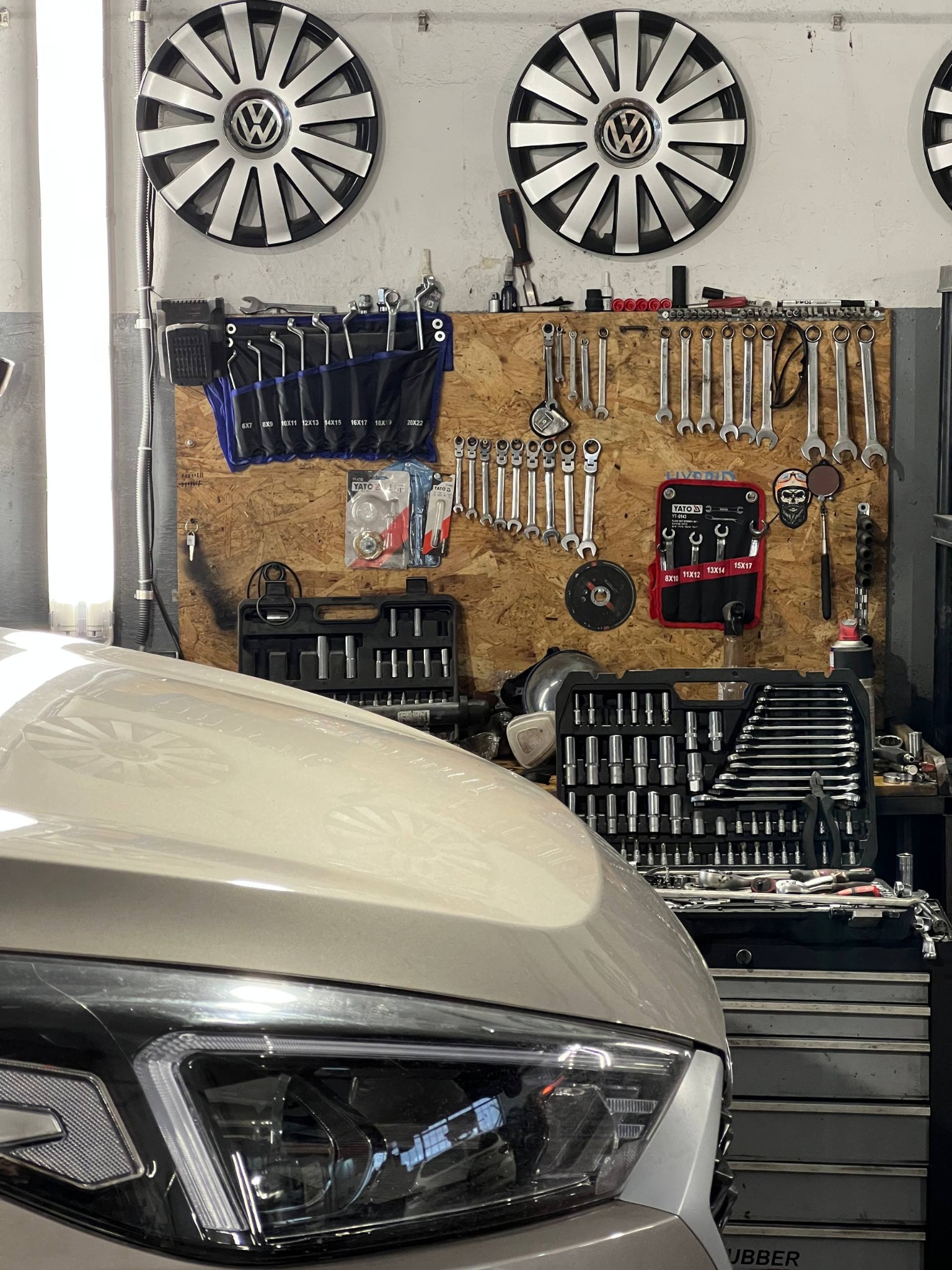 Reflektor auta na tle ściany warsztatu z narzędziami: klucze, nasadki, skrzynki narzędziowe i kołpaki VW. Warsztat samochodowy.