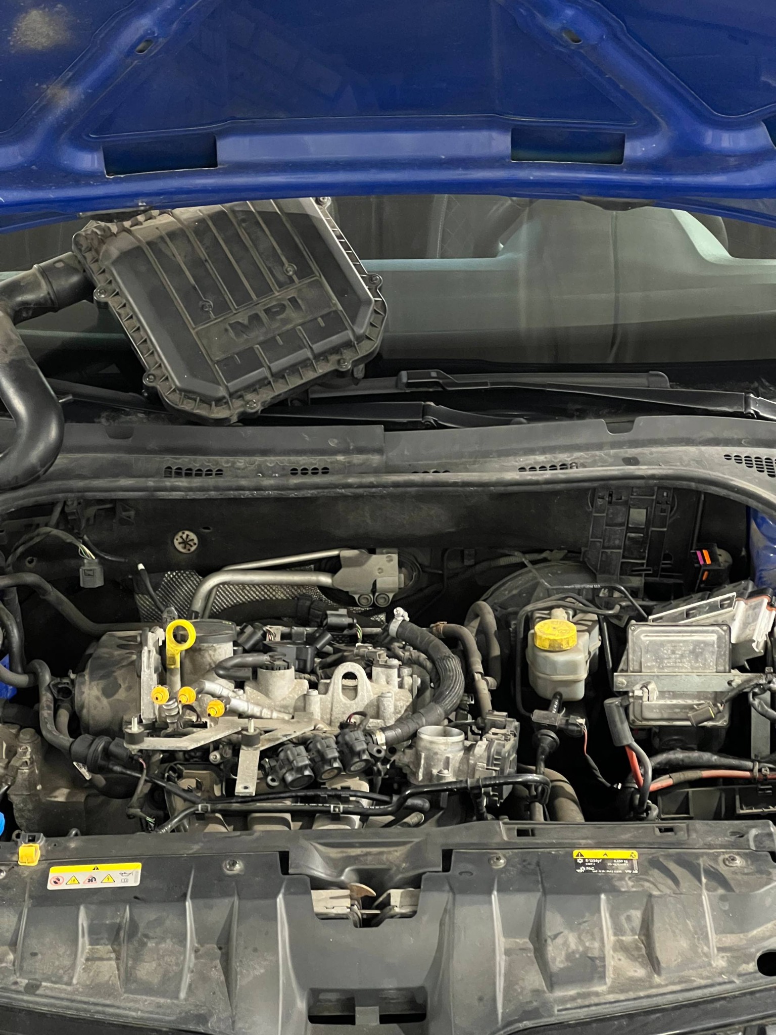 Otwarta maska samochodu w Katowicach, widoczny silnik z elementami układu dolotowego i płynów eksploatacyjnych. Diagnostyka w toku, widoczne żółte oznaczenia.