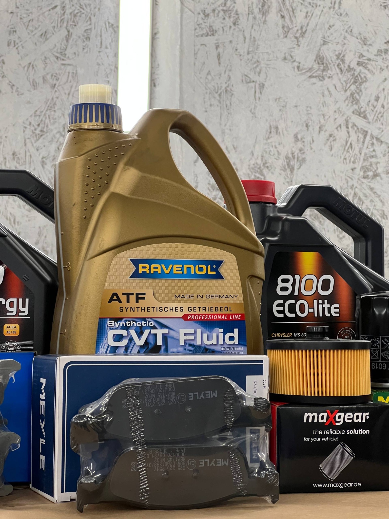 Olej silnikowy Ravenol ATF CVT Fluid, filtry oleju Maxgear i klocki hamulcowe Meyle na tle ściany. Produkty do serwisu i naprawy samochodów osobowych.