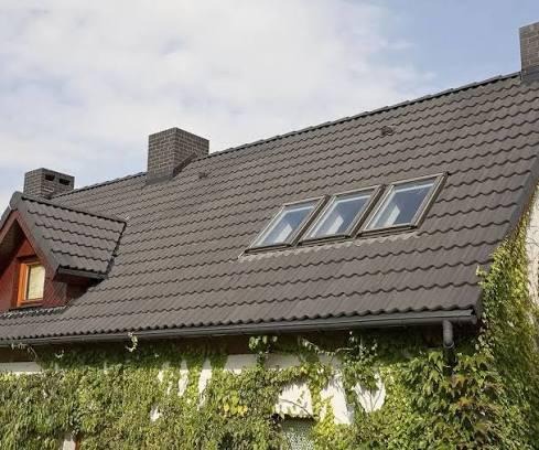 Ciemny dach z dachówką ceramiczną, trzema oknami dachowymi i ceglanym kominem. Rynna wzdłuż okapu, ściana budynku porośnięta bluszczem.