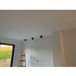 Hołyst - Wnętrze po malowaniu w Kątach: białe ściany, czarne lampy sufitowe, drabina przy oknie. Minimalistyczny styl, świeżo po remoncie.
