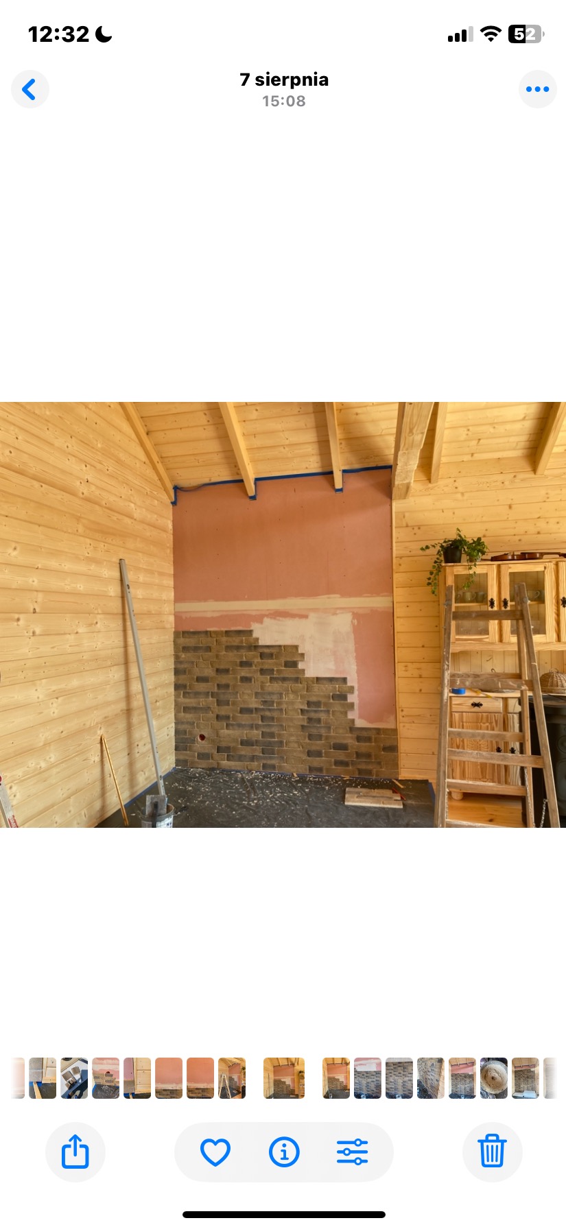 Wnętrze z drewnianymi ścianami w trakcie prac: częściowo ułożona dekoracyjna cegła na ścianie, widoczne narzędzia i drabina. Prace wykończeniowe w pomieszczeniu.