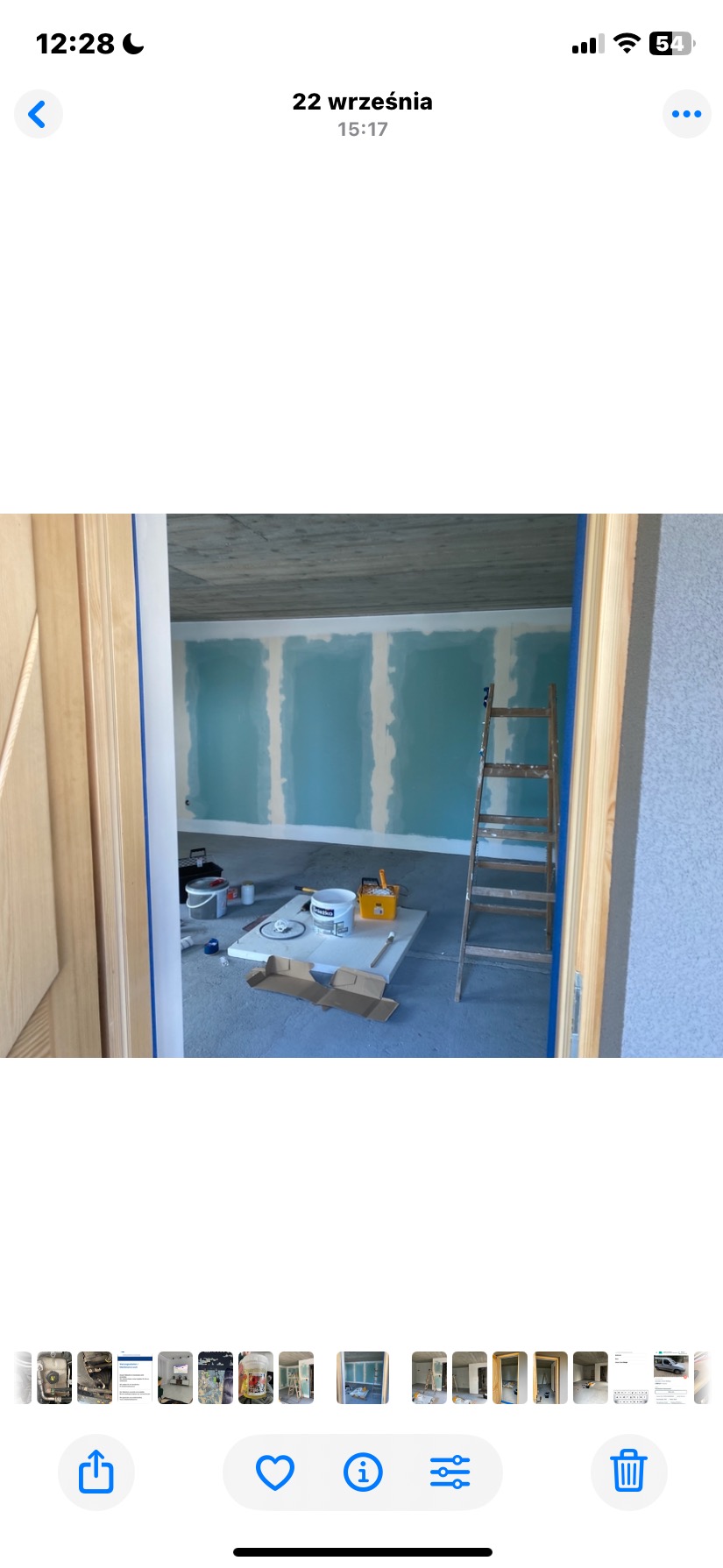 Wnętrze w trakcie prac: ściany z płyt gipsowo-kartonowych pomalowane na niebiesko, drabina oparta o ścianę, widoczne narzędzia i materiały malarskie. Surowy betonowy sufit.