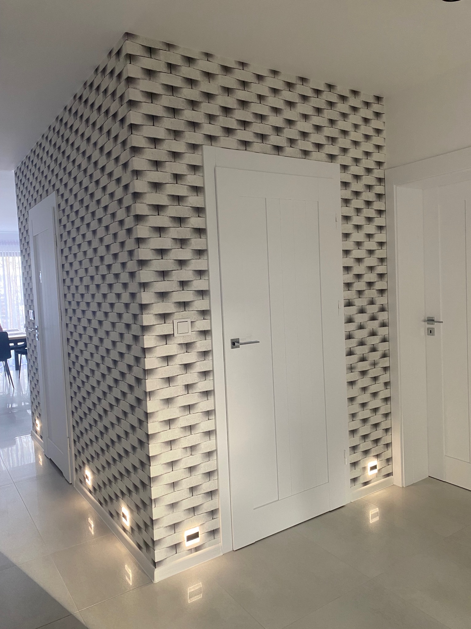 Korytarz z tapetą imitującą cegłę 3D, oświetleniem podłogowym i białymi drzwiami. Nowoczesne wykończenie wnętrza z dbałością o detale.