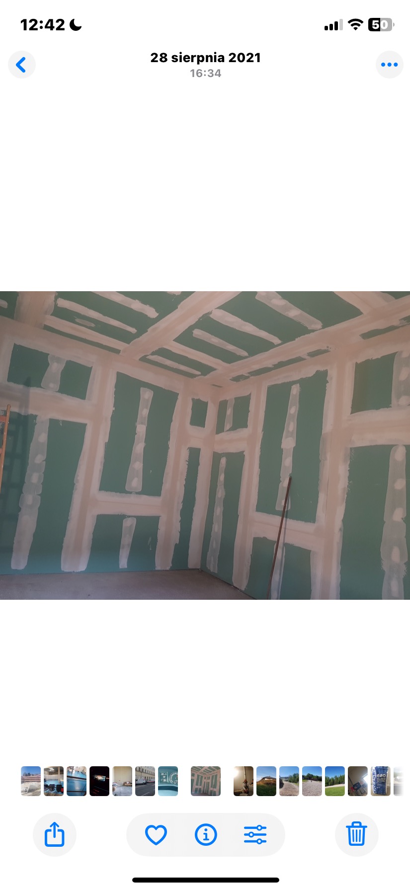 Ściany i sufit w trakcie przygotowania do malowania, pokryte zieloną farbą i białymi pasami szpachli, widoczne elementy konstrukcyjne. W tle drabina.