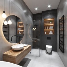 GLAZART - Glazurnictwo Remonty Wykończenia - Nowoczesna łazienka z szarymi płytkami, okrągłym lustrem z podświetleniem LED, drewnianą szafką pod umywalką i kabiną prysznicową ze szklaną ścianką.