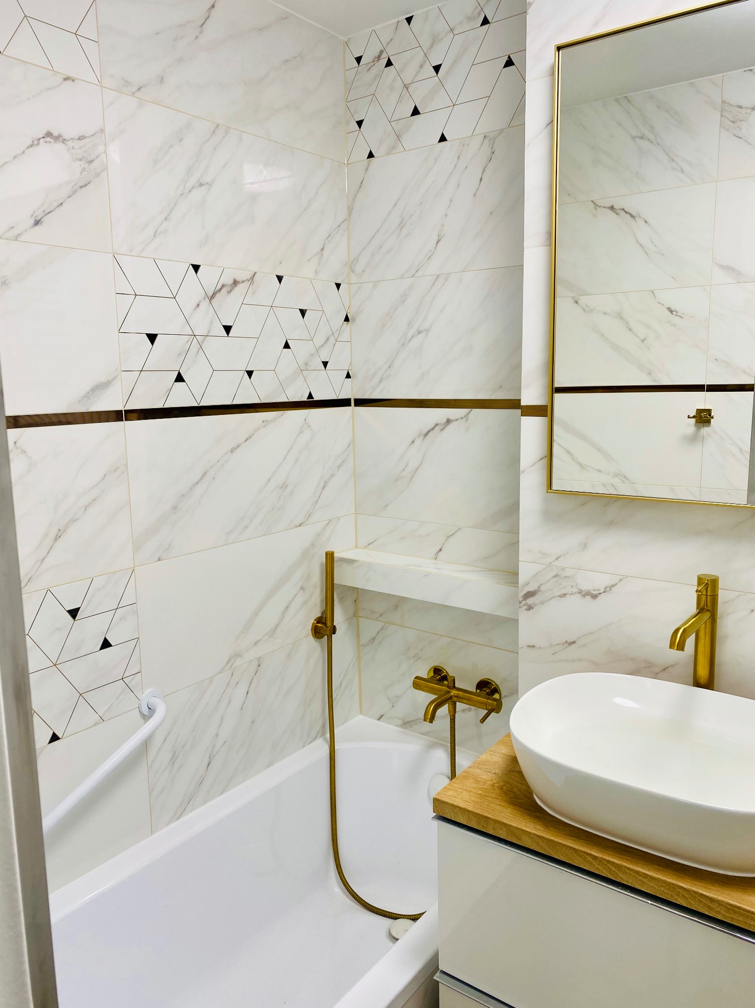 Wykończona łazienka w Wyszkowie: białe płytki imitujące marmur z geometrycznym wzorem, złota armatura, owalna umywalka nablatowa i lustro w złotej ramie.