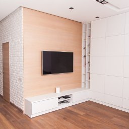 A-PROject Alexandr Karpeliov - Nowoczesny salon z ceglaną ścianą, drewnianą podłogą i minimalistyczną zabudową meblową w bieli. Telewizor na ścianie, subtelne oświetlenie.