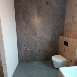 A-PROject Alexandr Karpeliov - Łazienka w trakcie wykańczania: szare płytki imitujące marmur na ścianach i podłodze, częściowo obudowana toaleta, surowy stan ścian w górnej części.